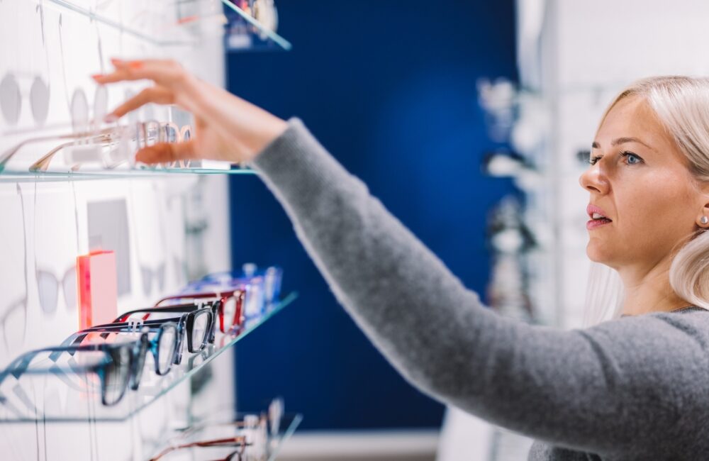 Naishenkilö optikkoliikkeessä valitsemassa hyllystä kehyksiä.