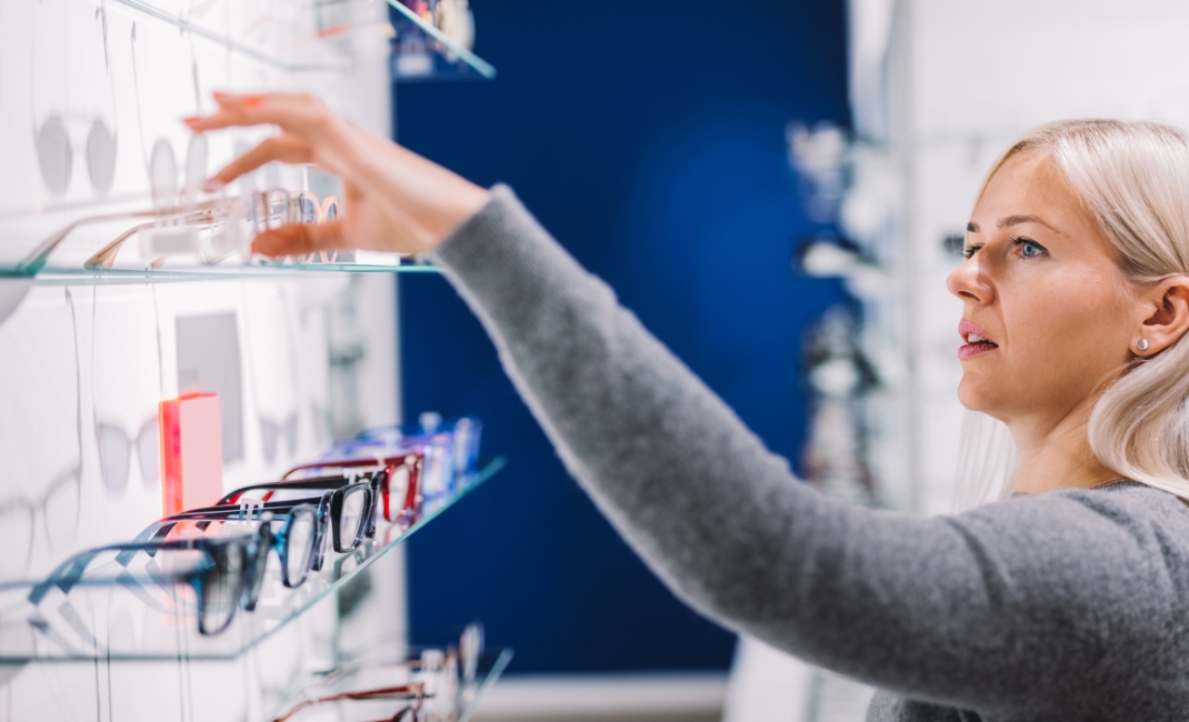 Naishenkilö optikkoliikkeessä valitsemassa hyllystä kehyksiä.
