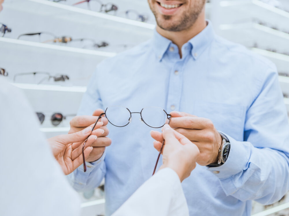 Optikko ojentaa miehelle silmälasit optikkoliikkeessä.