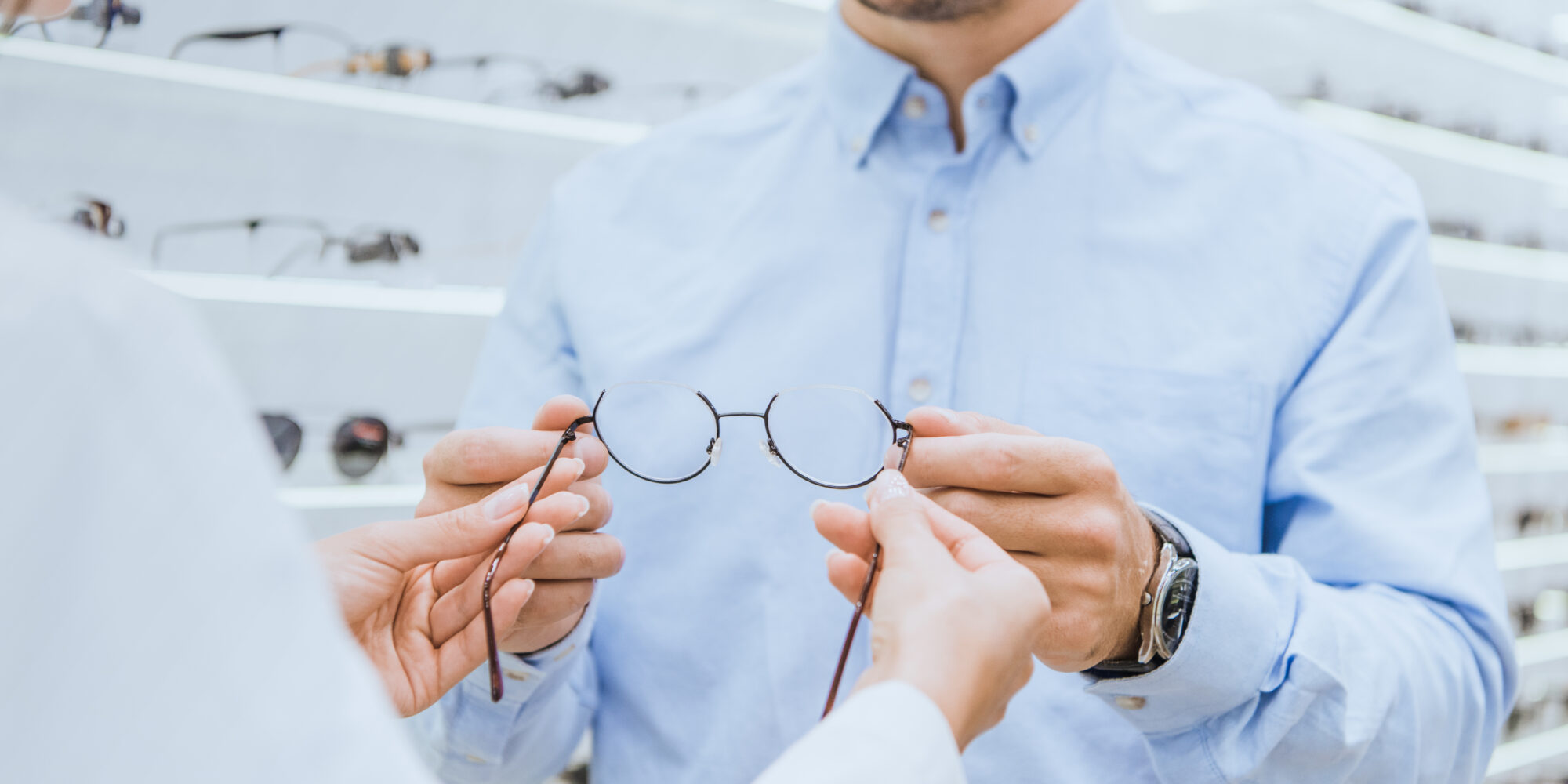 Optikko ojentaa miehelle silmälasit optikkoliikkeessä.