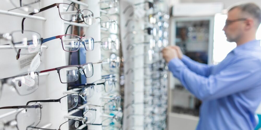 Keski-ikäinen mies katsoo silmälasivalikoimaa optikkoliikkeessä.