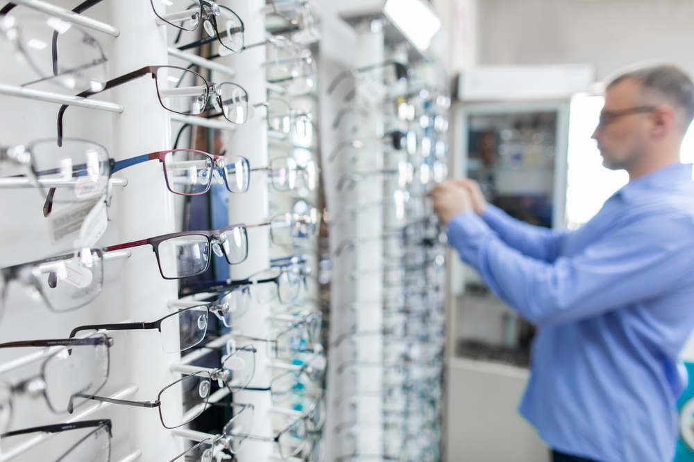 Keski-ikäinen mies katsoo silmälasivalikoimaa optikkoliikkeessä.