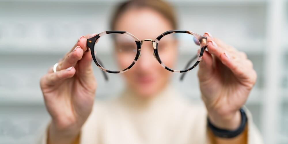 Nainen pitelee silmälaseja käsissään optikkoliikkeessä.