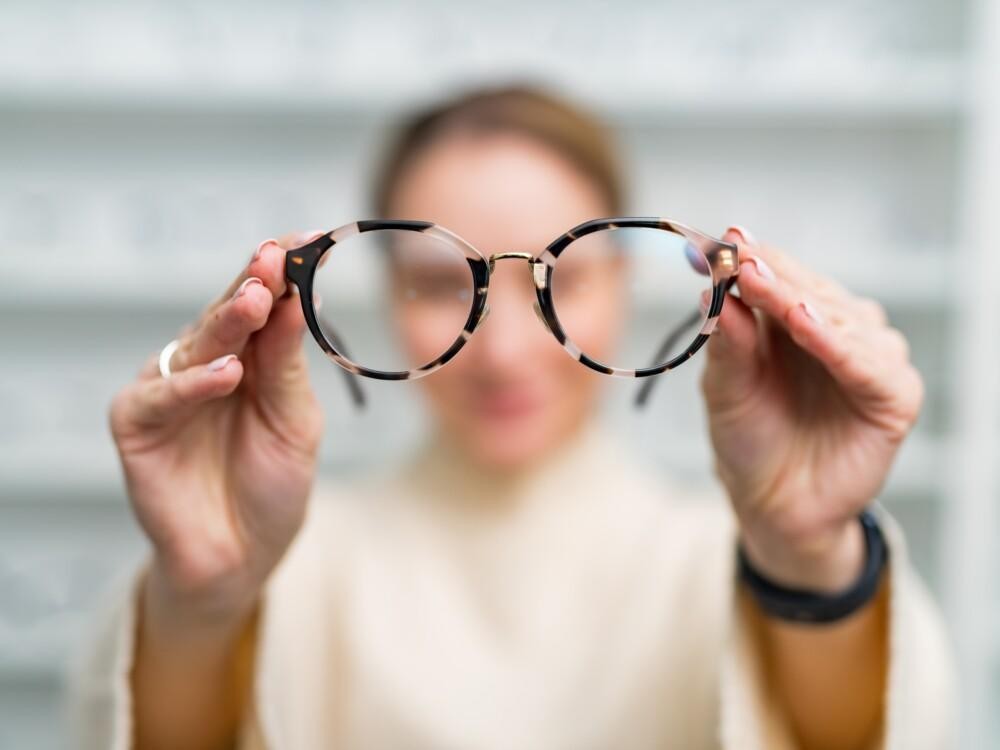 Nainen pitelee silmälaseja käsissään optikkoliikkeessä.